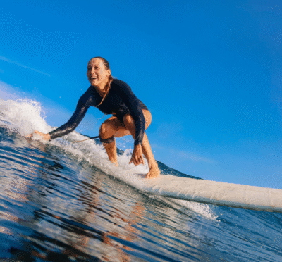 Surfer riding a wave in Honolulu with blue ocean water and a sunny Hawaiian sky in the background.