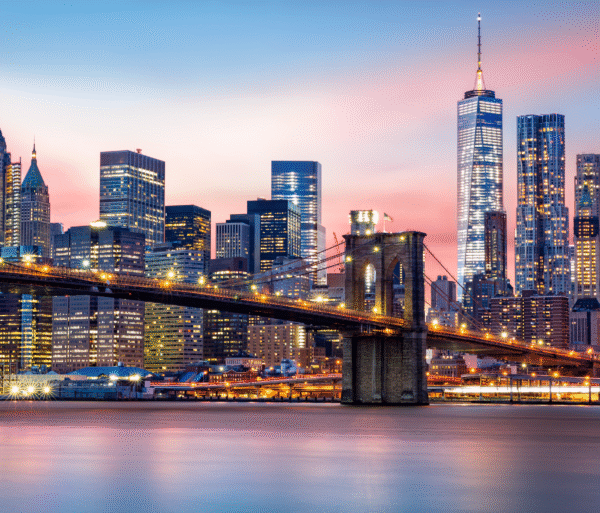 New York City skyline at sunset with a bridge in the foreground and golden light reflecting off the buildings.