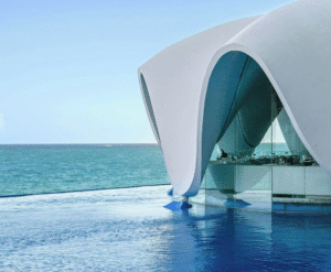 Infinity pool overlooking a sandy beach and turquoise ocean with palm trees swaying nearby