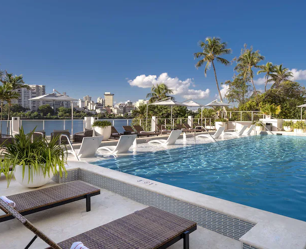Resort pool in San Juan surrounded by palm trees and lounge chairs under bright tropical sunshine