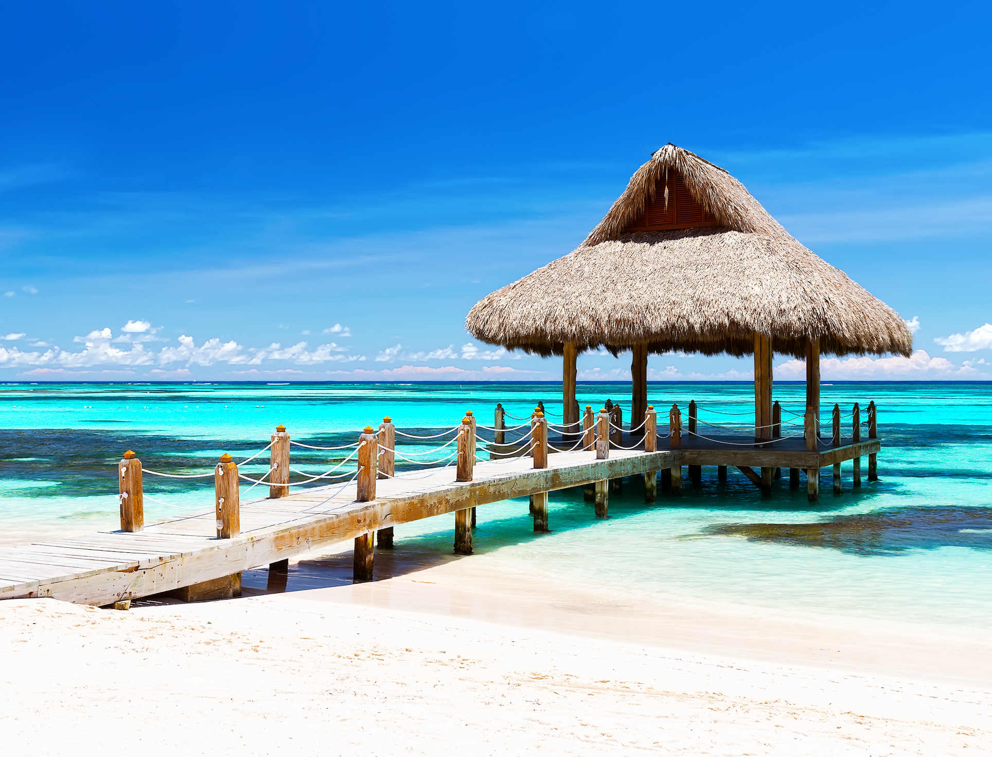 Wooden dock extending into turquoise water with a tiki hut at the end