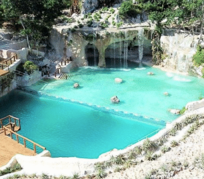 Vibrant blue cenote at Scape Park surrounded by rocky cliffs and greenery