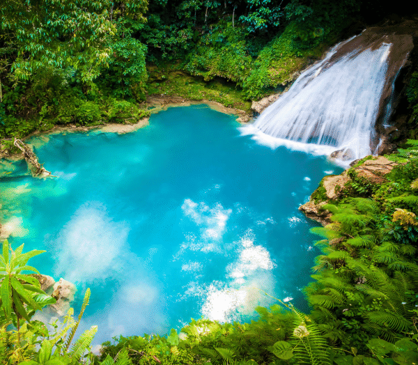 Waterfall cascading into bright blue pool surrounded by lush greenery in Jamaica