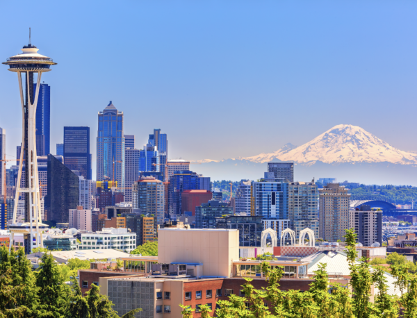 Seattle skyline at sunset with modern skyscrapers reflected in Elliott Bay and distant mountains in the background