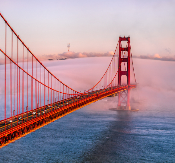 Golden Gate Bridge with orange towers rising above the water and light fog