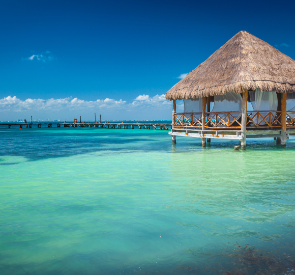 Thatched tiki hut perched over calm turquoise water in Cancun