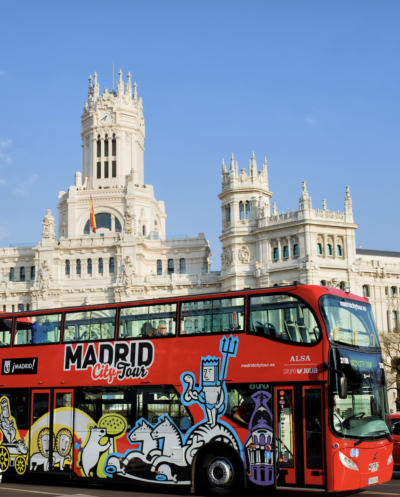 Double-decker sightseeing bus traveling through central Madrid past famous landmarks
