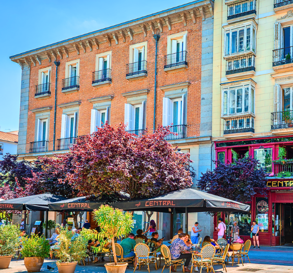 Outdoor seating area of a cozy Madrid café with tables, chairs, and a lively street atmosphere