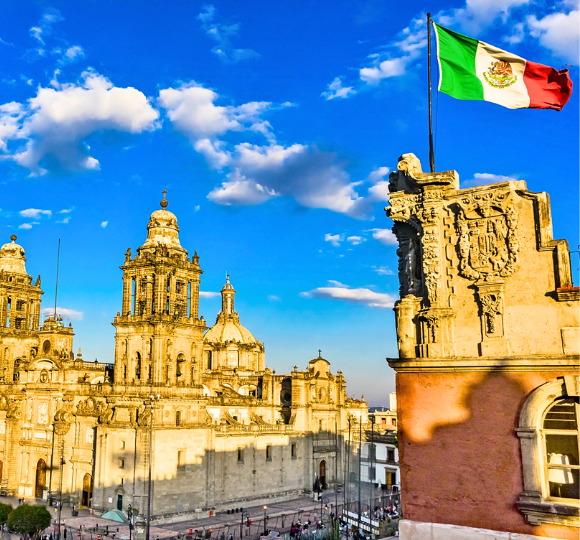 Mexico City skyline featuring historic architecture with the Mexican flag waving prominently above the city.