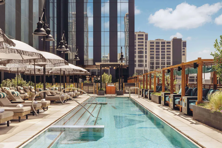 Thompson Austin hotel, where you can see the beautiful Austin, TX skyline, blue skies, surrounded by boutique-style loungers and umbrellas.