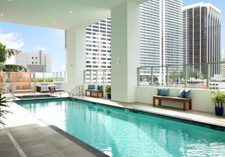 Yotel Miami pool overlooking the Miami skyline with blue skies and palm trees.